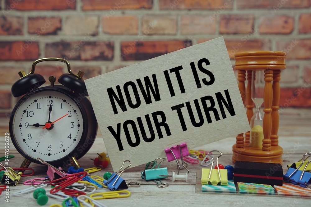 Poster now it is your turn text on paper card with alarm clock and stationary on wooden background