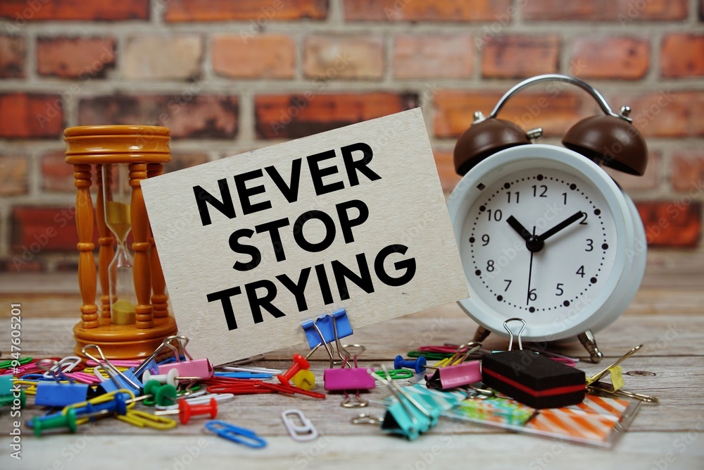 Poster never stop trying text on paper card with alarm clock and stationary on wooden background
