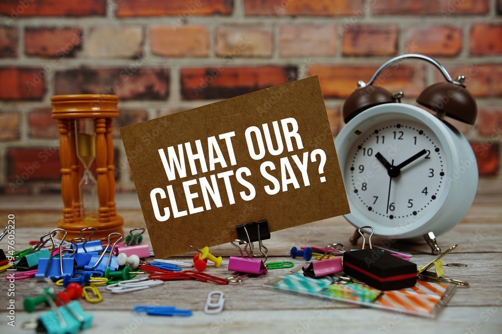 Poster what our clients say? text on paper card with alarm clock and stationary on wooden background