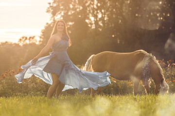 A young woman wearing a dress and her haflinger horse mare in front of a beautiful summer sunset...