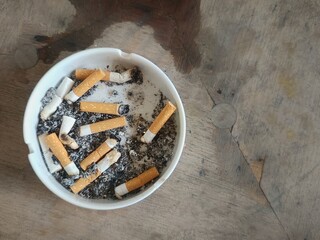 A white cigarette with a red filter rests in a ceramic ashtray, filled with ash and cigarette...