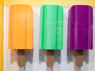 Artistic Representation of Three Yellow, Green and Purple Popsicles Hanging from the White Wall