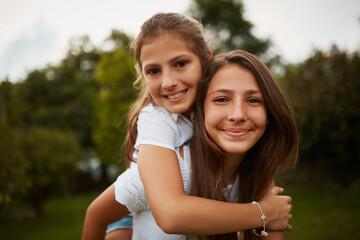 Fototapeta premium Girls, portrait and piggyback in park for bonding, love and support with trust, relationship and growth. Children, face and family outdoor in nature for laugh, playing and development with carrying