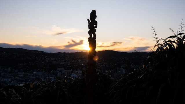 Silhouetted cultural Maori pou whenua carved statue on Mt Victoria lookout against sunset sky in capital city of Wellington, New Zealand Aotearoa - taken on 5th August 2024