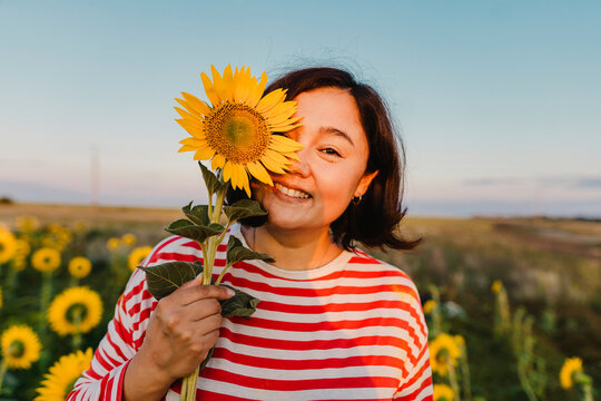 Smiling mature woman covering half face with sunflower in field