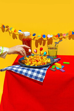 Woman's hand picking up fast food french fries from plate on table against yellow background