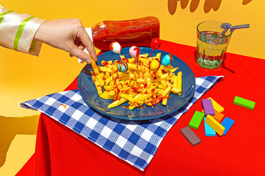 Woman's hand picking up unhealthy french fries from plate on table over yellow background