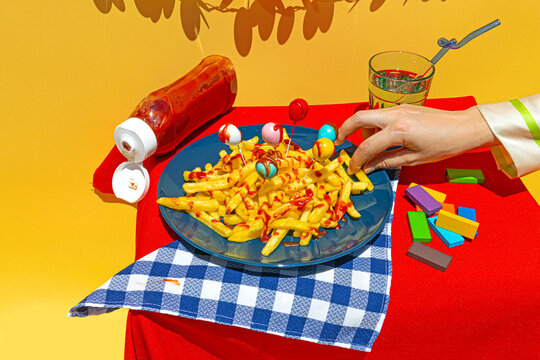 Hand of woman picking up unhealthy french fries from plate on table over yellow background