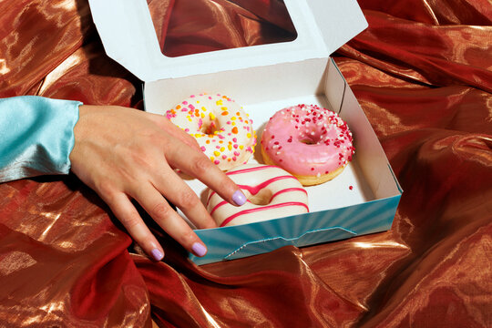 Woman picking up decorated donuts from box over iridescent cloth