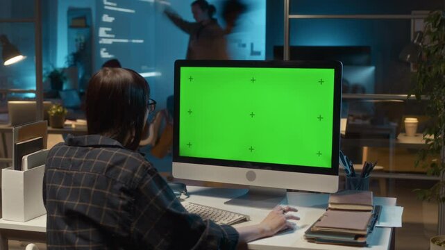 Timelapse back view of unrecognizable female database administrator sitting at desk with computer with green screen, IT office workflow in background