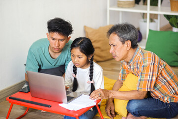 Side View Of Concentration Asian Family Teaching Little Girl Using Laptop On Table While Sitting on...