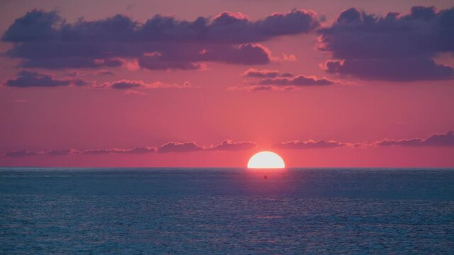 Beautiful evening colored sky, a calm sea along which one person is sailing, the sun close to the horizon
