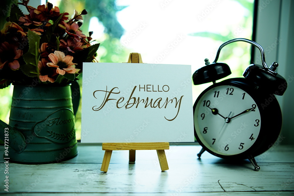 Aufkleber hello february text on paper card with easel and alarm clock in the window background