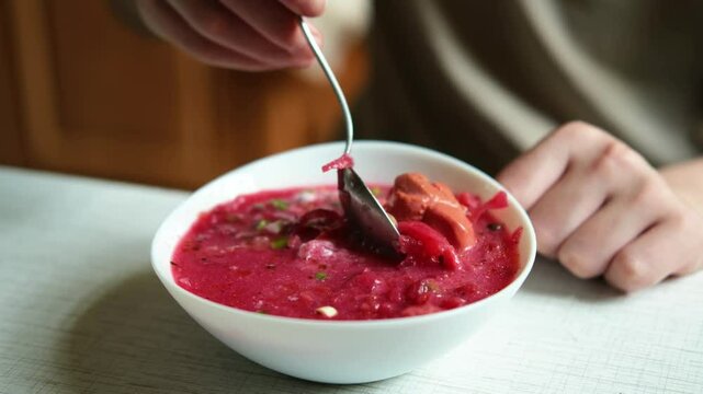 The hand of a man with a spoon takes borscht from the plate. The process of eating a home-cooked lunch.