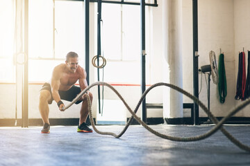 Battle rope, man and fitness in gym, challenge and cardio workout with exercise, training routine...