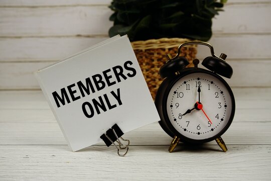 Members Only text message on sticky note with alarm clcok on wooden background