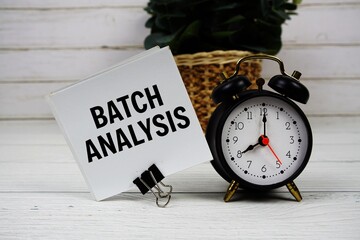 Batch analysis text message on sticky note with alarm clcok on wooden background