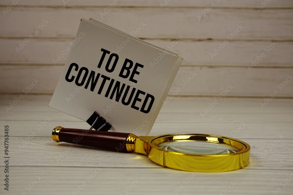 Poster to be continued text message on sticky note with magnifying glass on wooden background