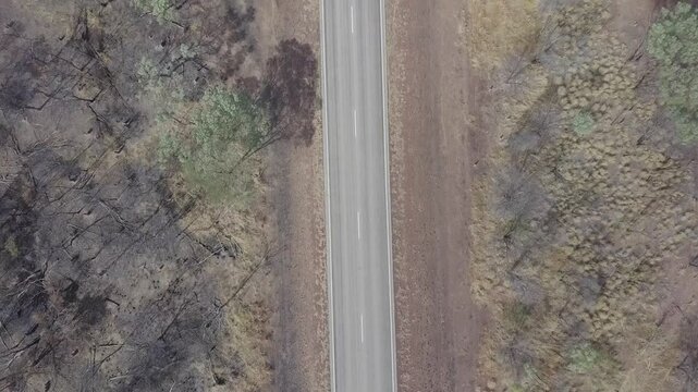 Aerial view of road train traveling along the straight Stuart Highway through barren wilderness and dry vegetation, Wilora, Australia.