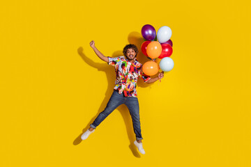 Full size photo of pretty young guy hold air balloons flying excited wear trendy colorful outfit isolated on yellow color background