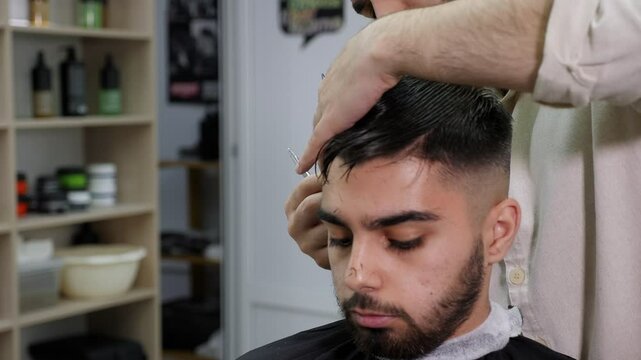 Close-up of a male barber cutting a client's hair in a modern barber shop. A professional hairdresser cuts a man's hair with scissors and a comb.