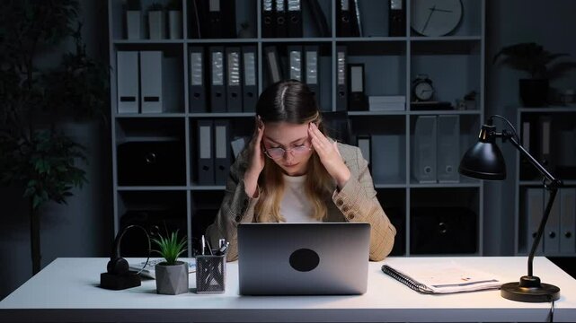 Upset and sick Caucasian young adult businesswoman suffering from migraine while working in the office. Concept of a upset, burnout, stress and crisis.