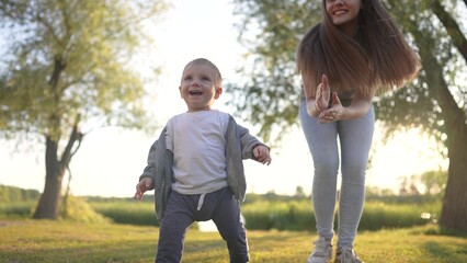 A baby is taking first steps in the grass. spring breastfeeding feet concept. a mom helps her baby with the first steps. lifestyle mom helps her baby with the first steps in the grass.