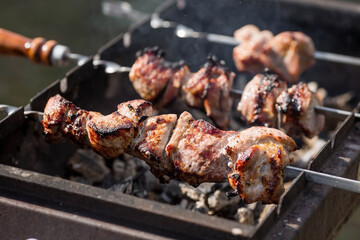 Pork kebab in the country in nature. May holidays. Pork kebab on skewers. The process of cooking meat on the grill with smoke, close-up.