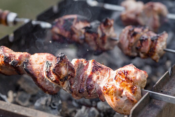 Pork kebab in the country in nature. May holidays. Pork kebab on skewers. The process of cooking meat on the grill with smoke, close-up.