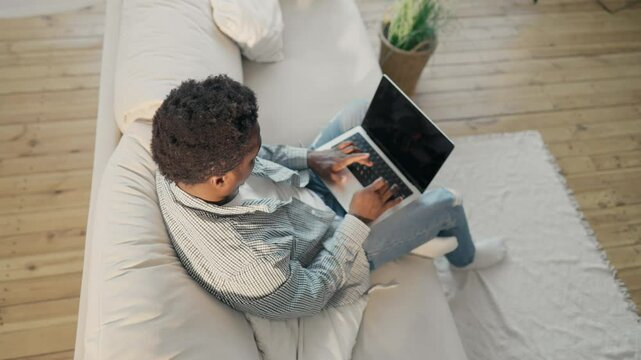 Black man with modern laptop at home, top view on male student in living room, Work online and shopping in web stores, African American male person using portable computer in flat, Wi-Fi connection