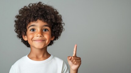 Poster for advertising, A young boy of african descent with curly hair is smiling and pointing up with his finger against a grey background; 