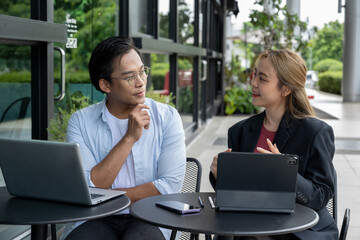 Two businessmen discussing work using tablets and laptops in a modern coffee shop.