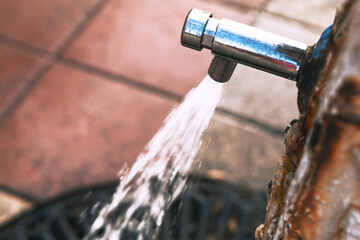 Faucet is dripping water onto a sidewalk. Water pipe leaks, dripping water steadily onto the ground...