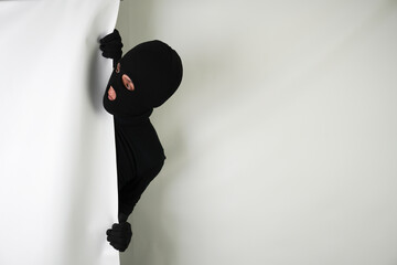 Young Adult black masked robber with gloves is Peeking from behind a wall. Isolated over white...
