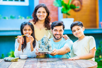 Indian family making eco-friendly Ganesh idol in outdoor garden for Ganesh Chaturthi celebration