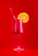 refreshing tropical cocktail glass of strawberry red fruits with orange slice on red background