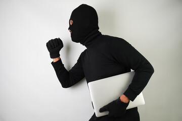 Young Adult black masked robber is holding silver colored laptop. Running, fleeing and escaping...