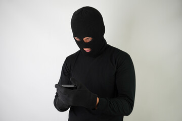 Young Adult black masked robber is holding smartphone with blank green screen and he calling his...