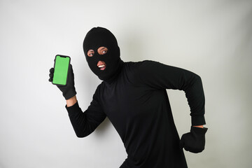 Young Adult black masked robber is holding smartphone with blank green screen. Running, fleeing and...