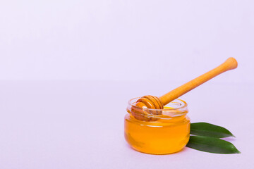 Honey in jar with leaves and honey dipper on colored background top view with copy text