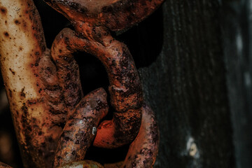 Rusty chain links hanging against a dark background near a wooden surface during low-light...