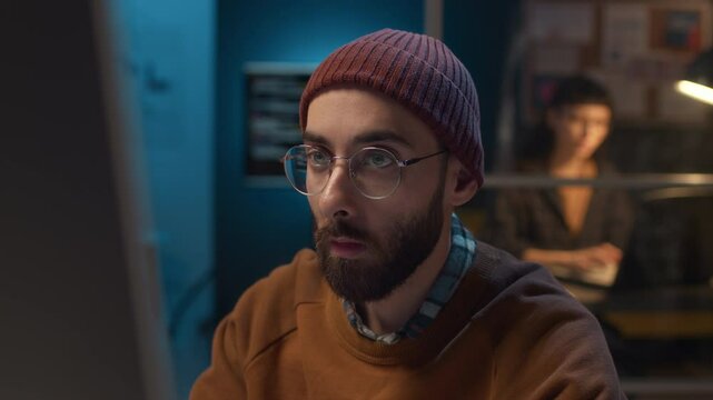 Close-up of face of young Caucasian man working in IT office sitting at desk providing remote technical support to users by resolving software issues