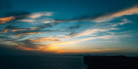 Orange and blue sunset sky with dramatic clouds over a Mediterranean sea coastline