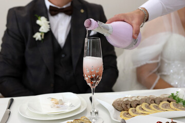 The glasses of the bride and groom are filled with sparkling wine at the festive table.