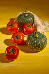 Food advertisement image with ingredients of mini pumpkins and fresh tomatoes placed in a net on the light wooden table. Minimalist space with autumn theme