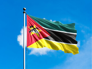 Mozambique flag flying on blur blue clouds background.