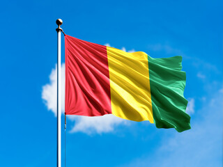 Guinea flag flying on blur blue clouds background.
