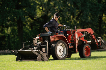 Sitting and driving. Man is with utility tractor with grass cutter and aerator equipment on the field