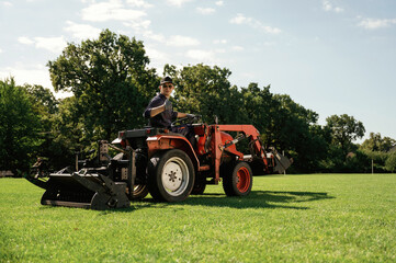 Man is with utility tractor with grass cutter and aerator equipment on the field