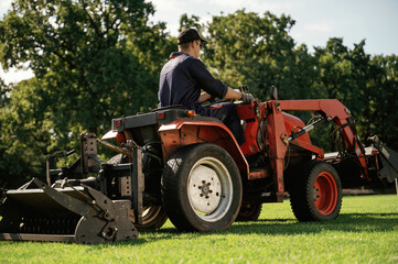 Sitting and driving. Man is with utility tractor with grass cutter and aerator equipment on the...